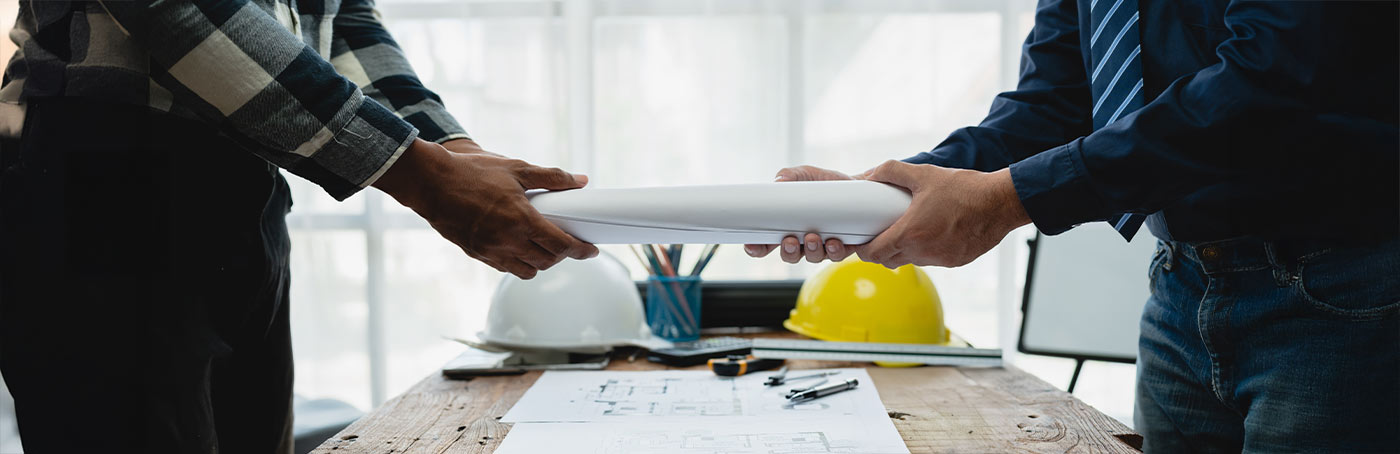 Picture of two men holding rolled up blueprints from across a table