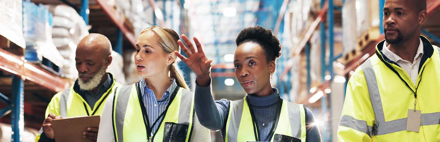 Close-up of a group of four diverse people in yellow vest walking through a warehouse together